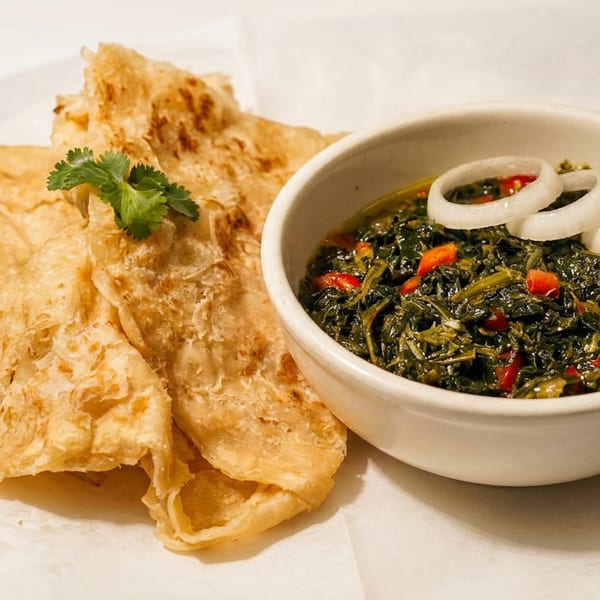 Bowl of stewed greens with onion rings and flatbread garnished with cilantro on white parchment paper.