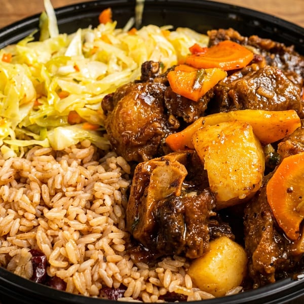 Stewed oxtail with rice and peas and cabbage in a black bowl on a wooden table.