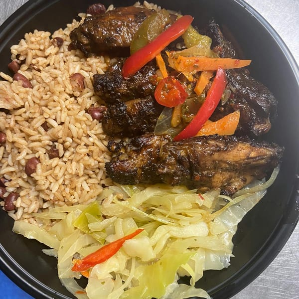 Jerk chicken with rice and peas, sautéed cabbage, and colorful peppers in a black bowl.