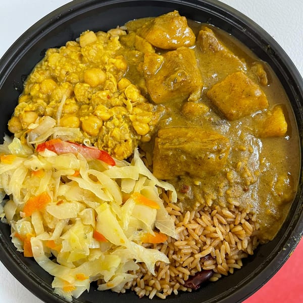 Curry chicken, chickpea stew, steamed cabbage, and rice and peas in a black takeout bowl.