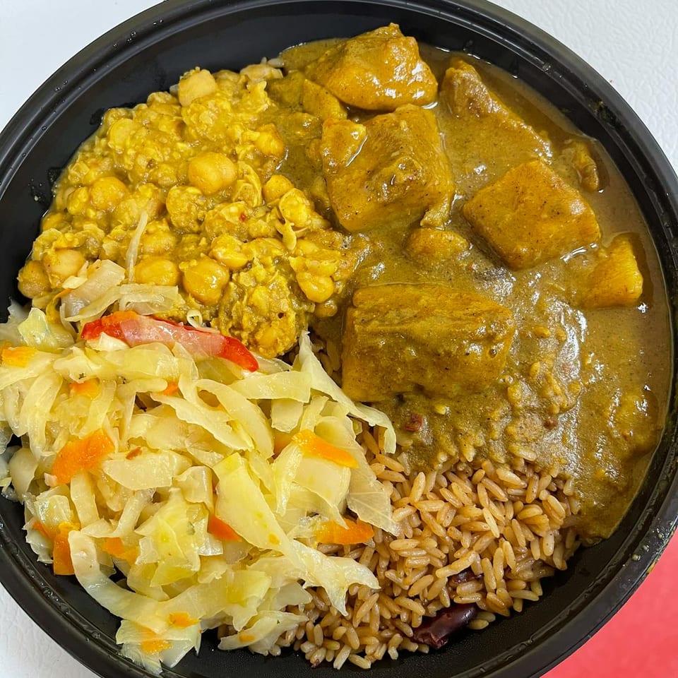 Black bowl with curry chicken, chickpea curry, rice and peas, and steamed cabbage.